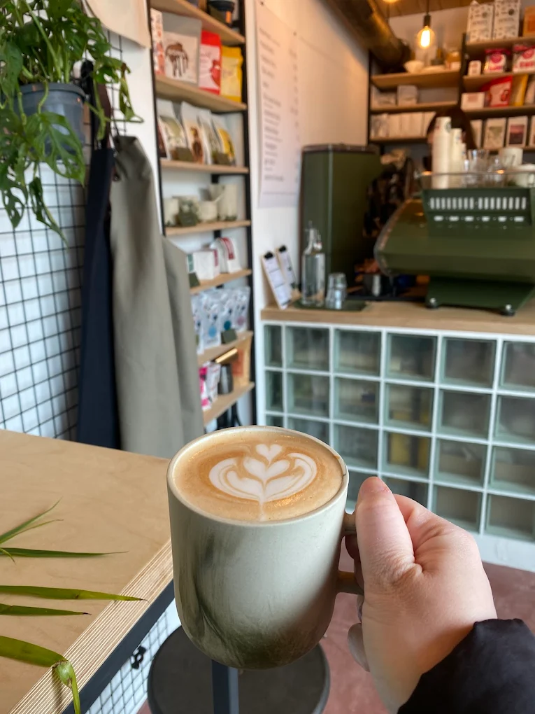 Ruka drží šálek latté s lístkovým latte artem