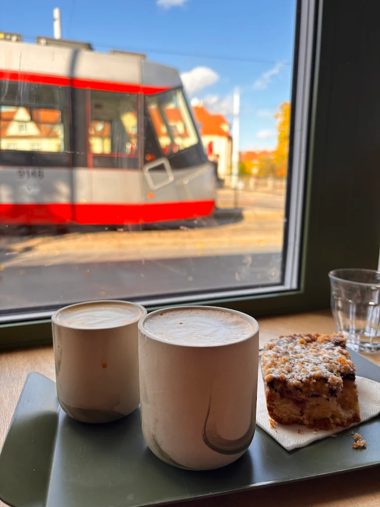 Dvě latté a kousek koláče u okna s projíždějící tramvají